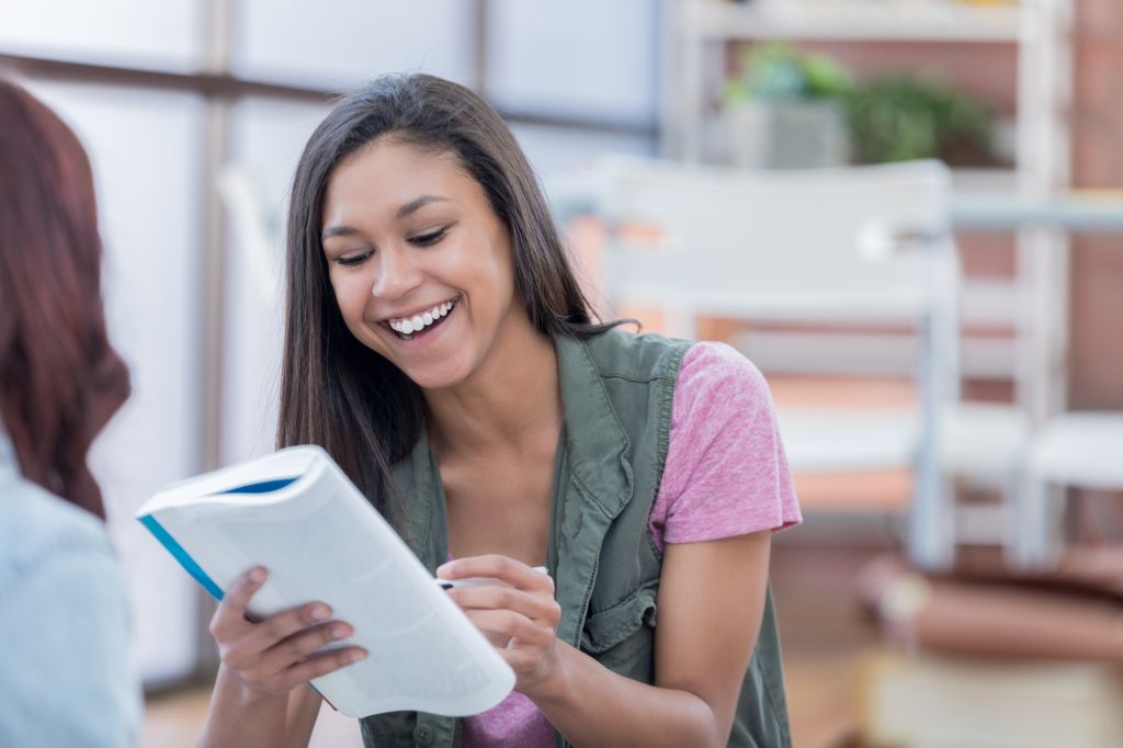 Smiling college student reads a book with her friend