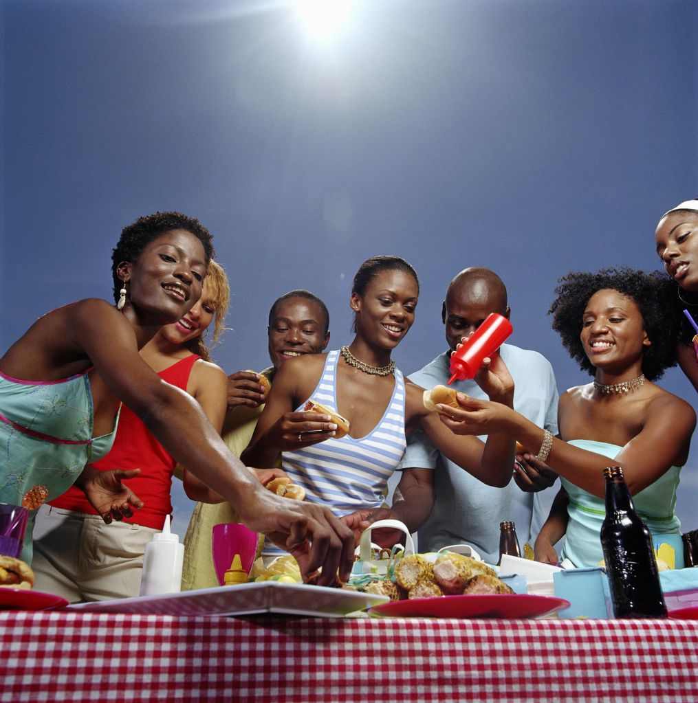 Group of friends gathered around table of food, outdoors