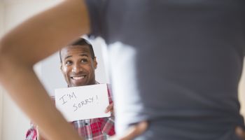 Man showing 'I'm Sorry' sign to angry girlfriend