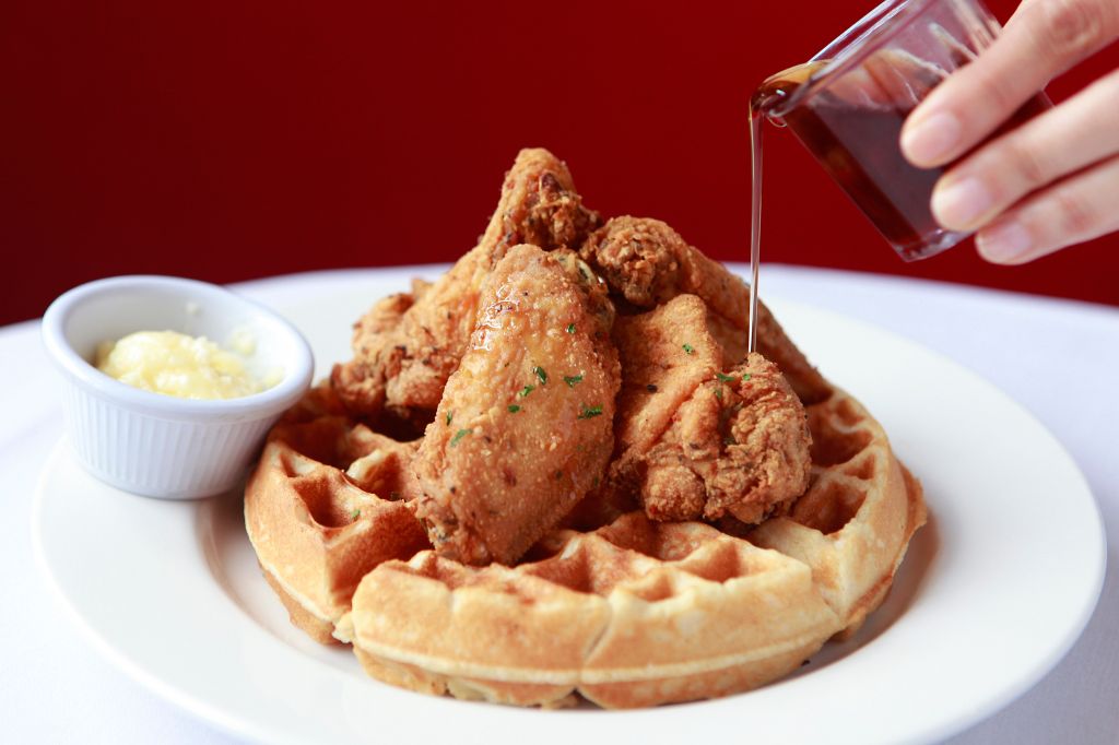 pouring syrup on fried chicken and waffles on restaurant table with butter