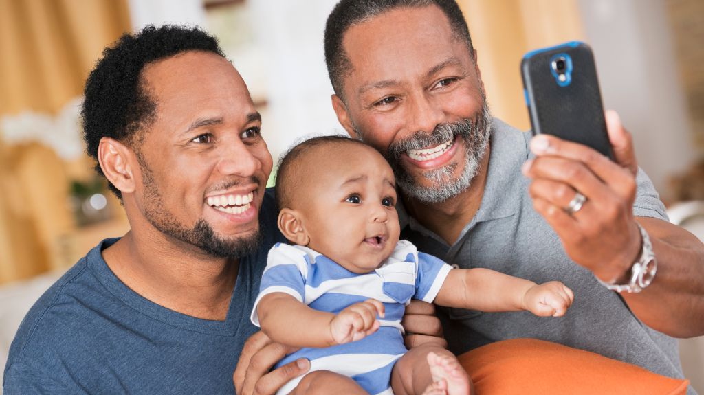 Black father and grandfather posing for cell phone selfie with baby boy