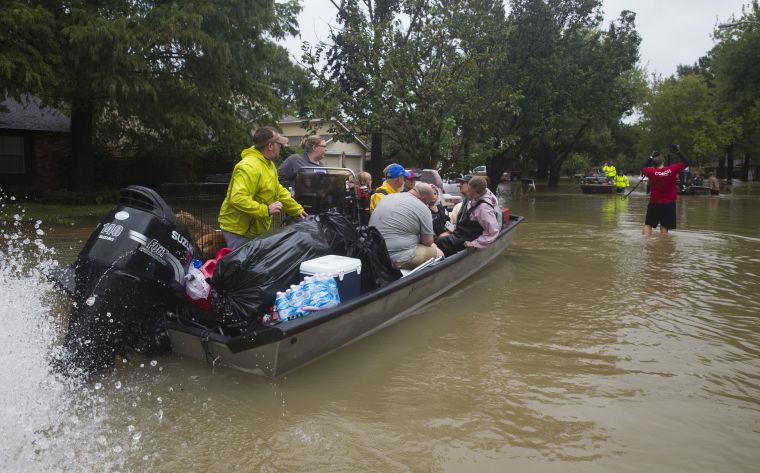 A large boat is pulled through shallow water in a flooded neighborhood.