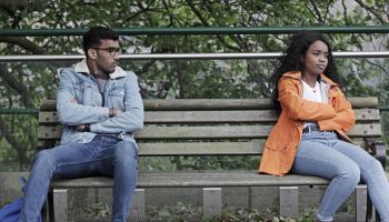 Man and woman sat at opposite ends of bench, not happy