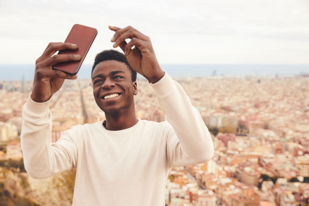 Happy man taking selfie through phone against city