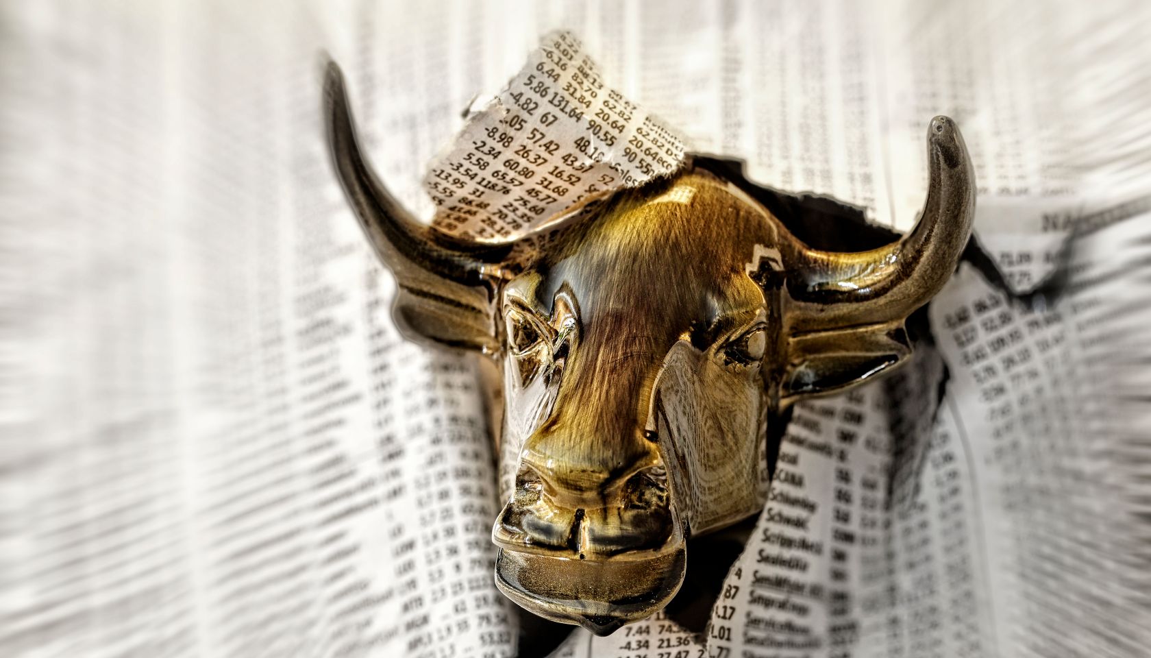 Bull looking through torn page of newspaper