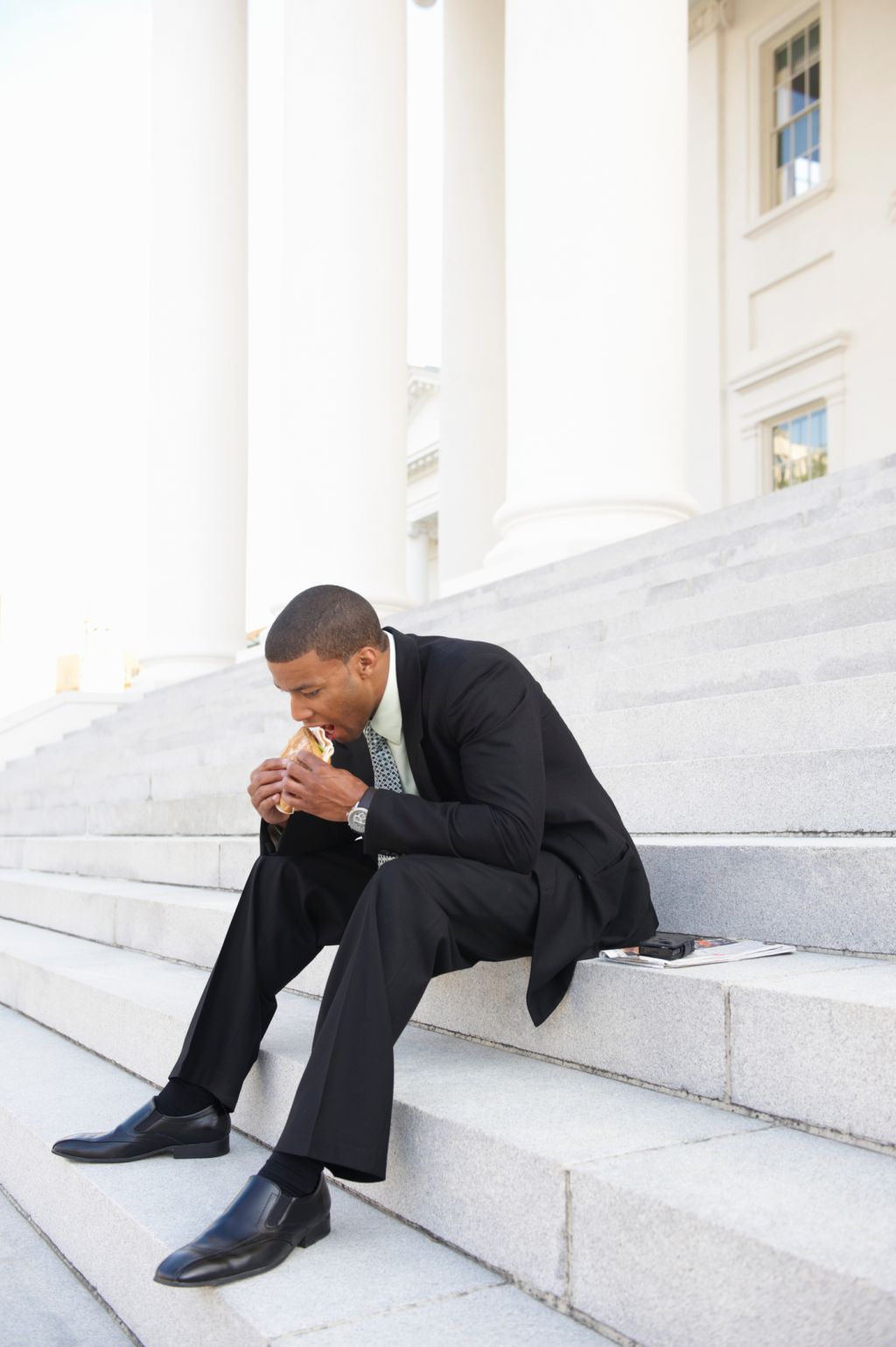 African American businessman eating sandwich on courthouse steps