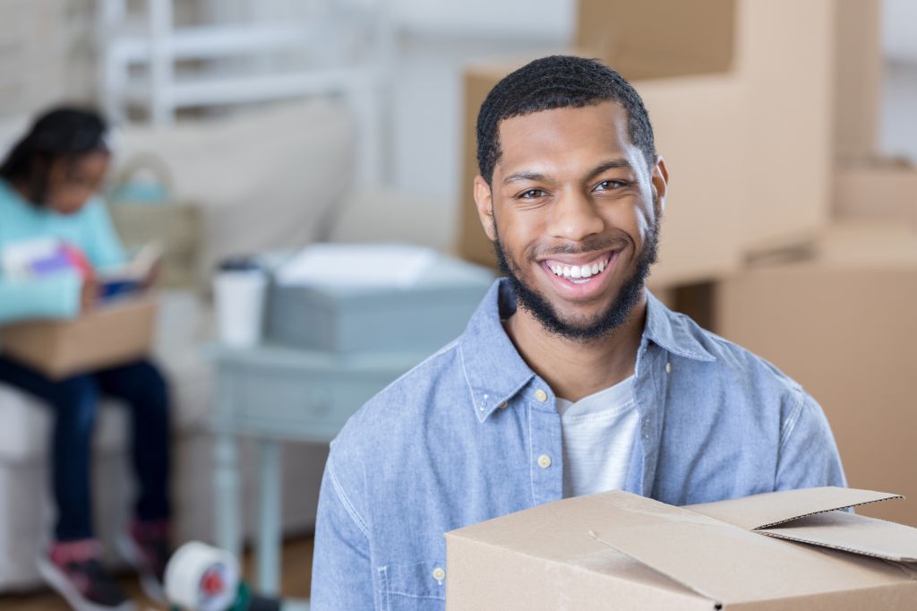 Young man smiles for camera while holding moving box