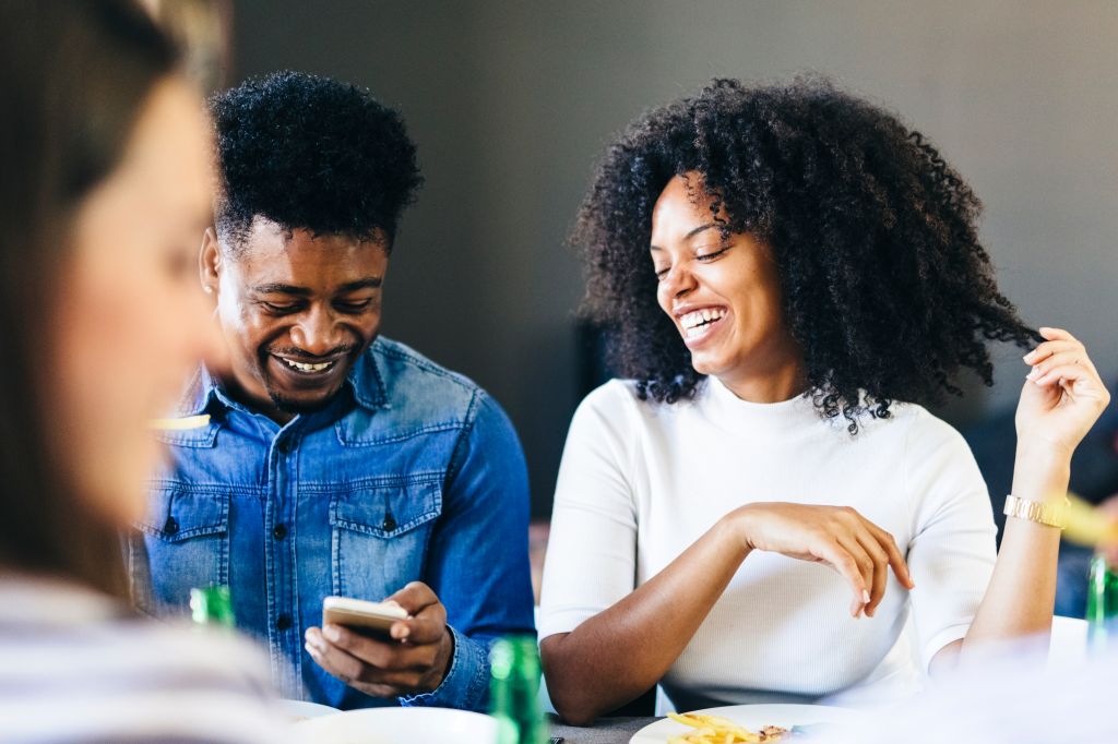 Happy couple sharing cell phone at dining table
