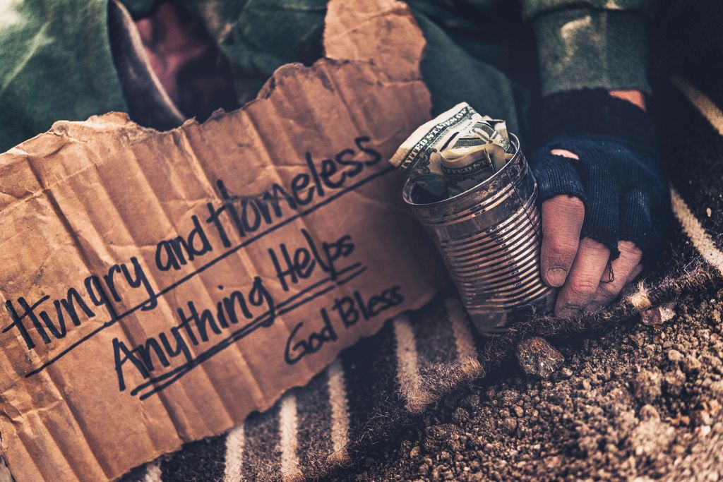 Fighting adversity. Homeless man sleeping with sign and money tin