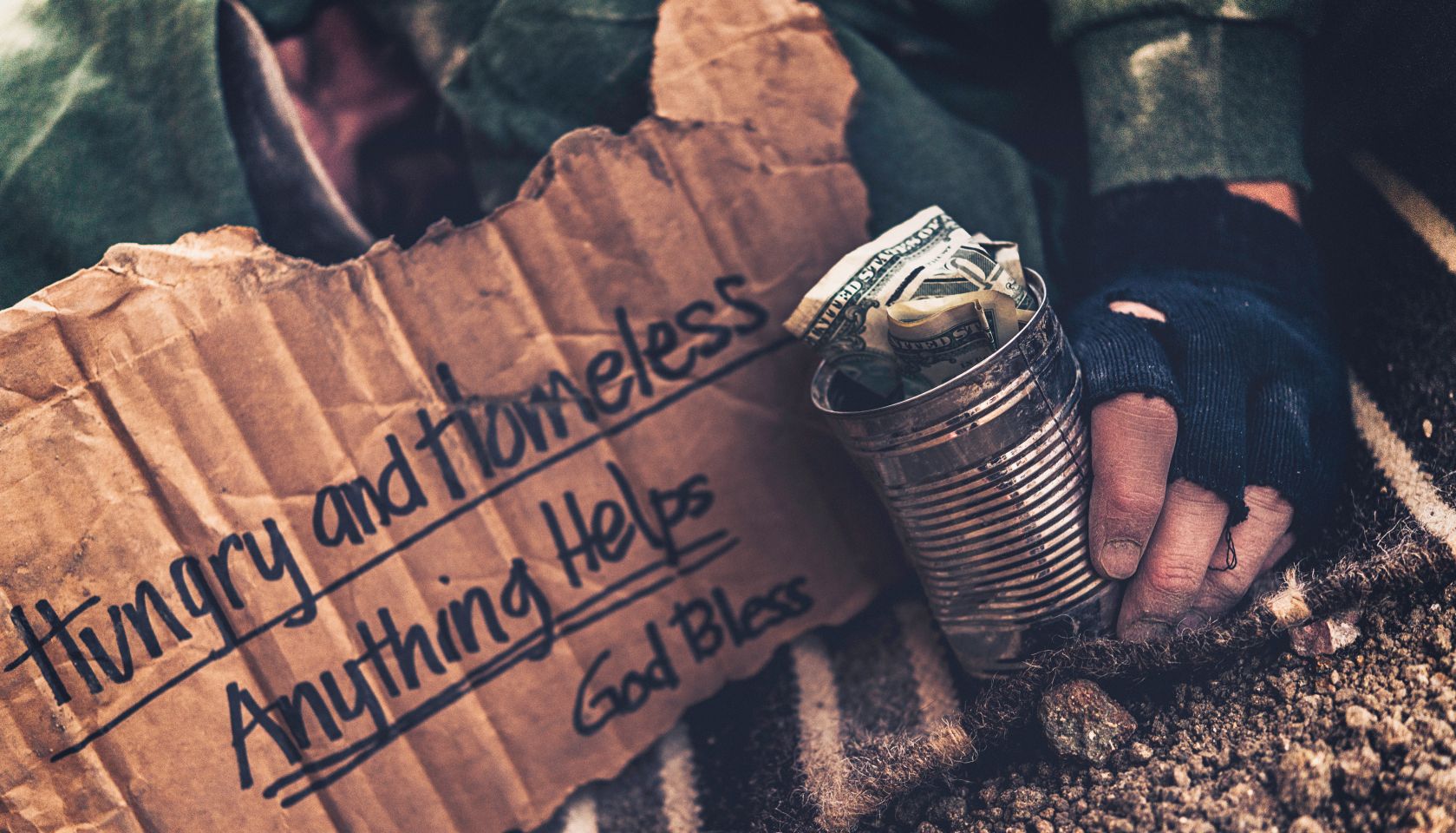 Fighting adversity. Homeless man sleeping with sign and money tin