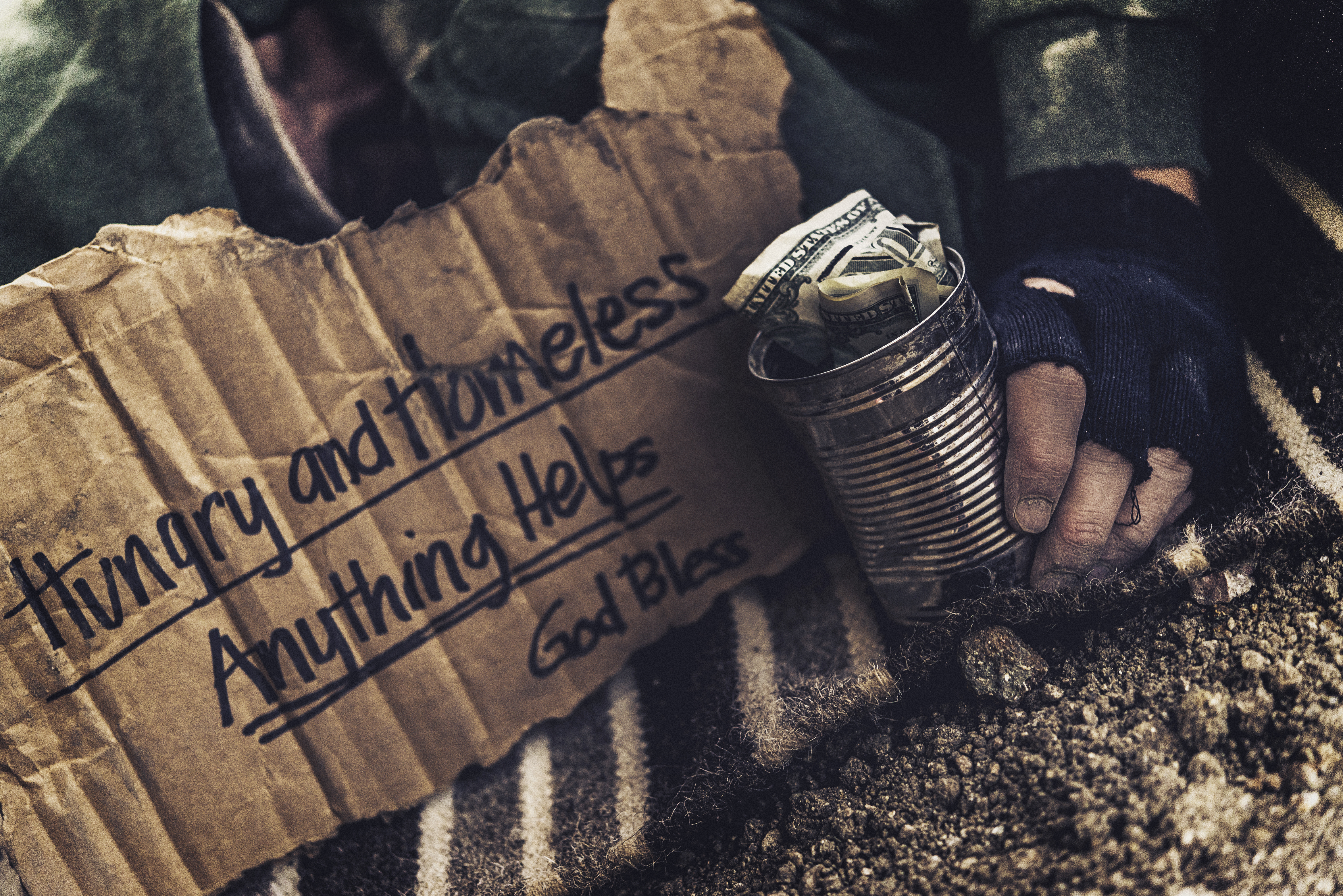 Fighting adversity. Homeless man sleeping with sign and money tin