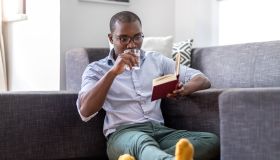 Young man sitting on the floor in the living room reading book and drinking glass of water