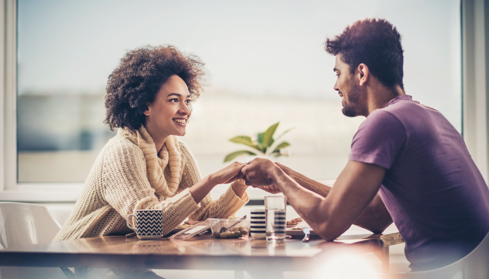 Loving black couple holding hands while having a lunch by the window.