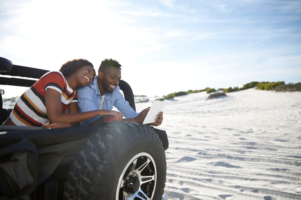 Couple with digital tablet in jeep on beach