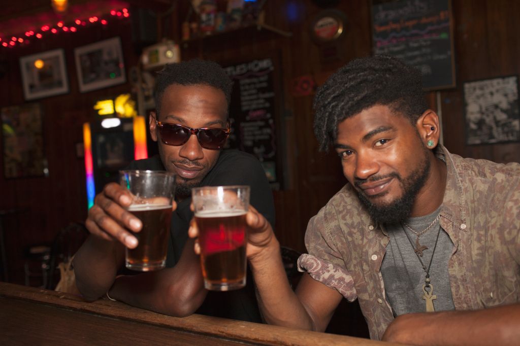 Two young men toasting at a bar.