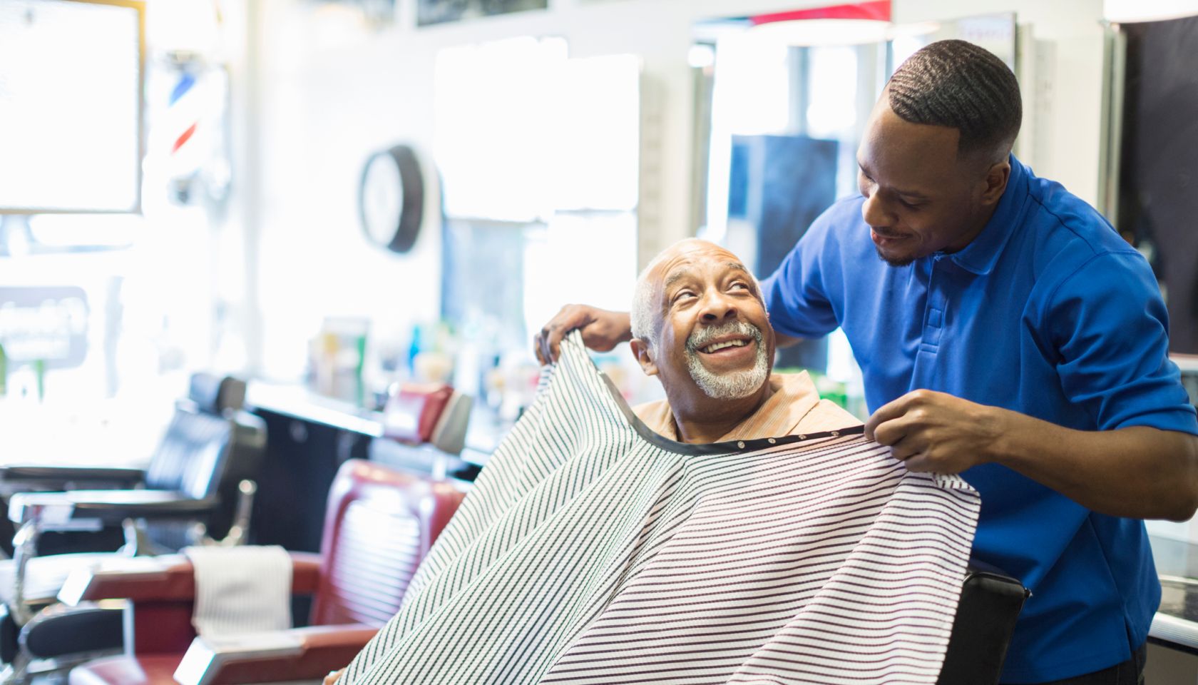 Black barber tying apron on customer in retro barbershop