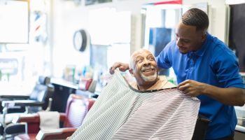 Black barber tying apron on customer in retro barbershop