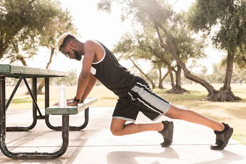 Black man leaning on picnic table in park stretching legs