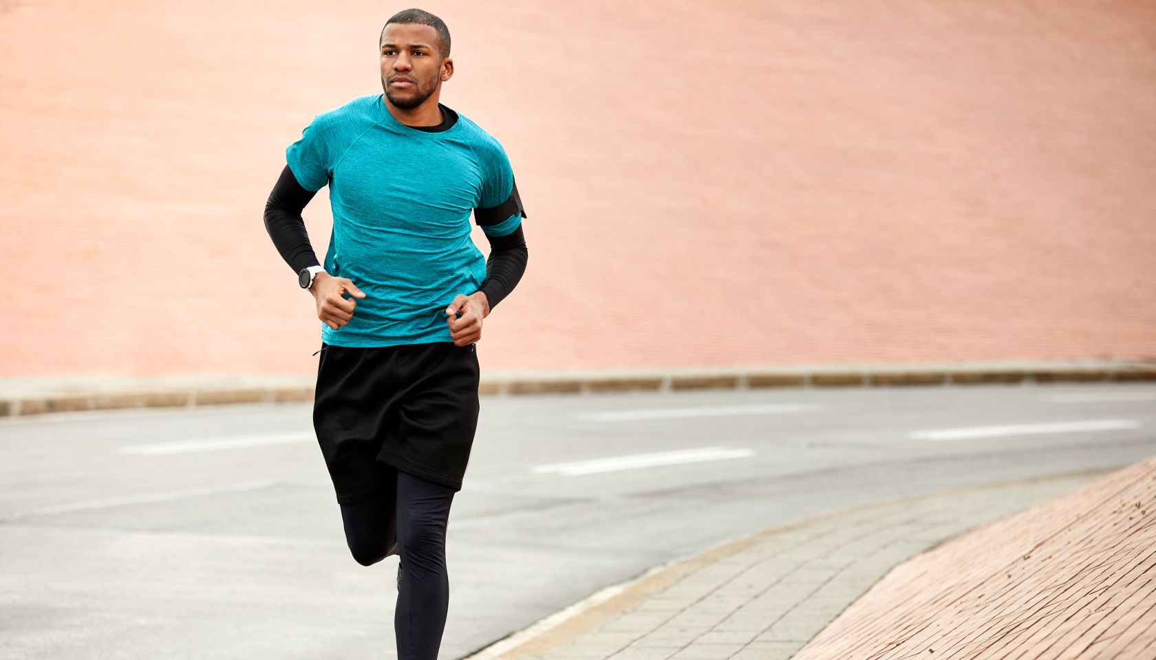 Young man jogging on roadside against wall in city