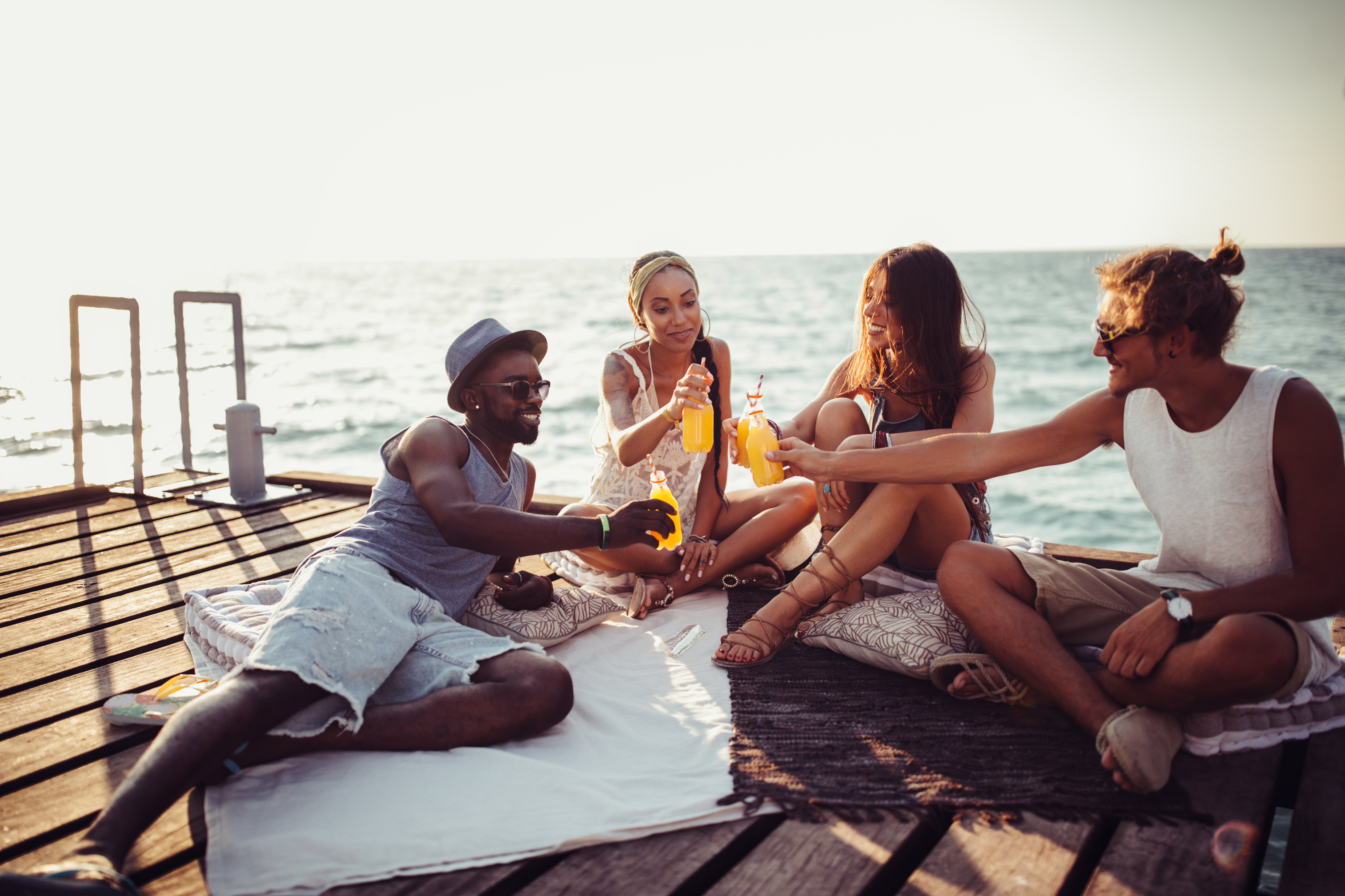 Multi-ethnic friends drinking soda and having beach party on jetty