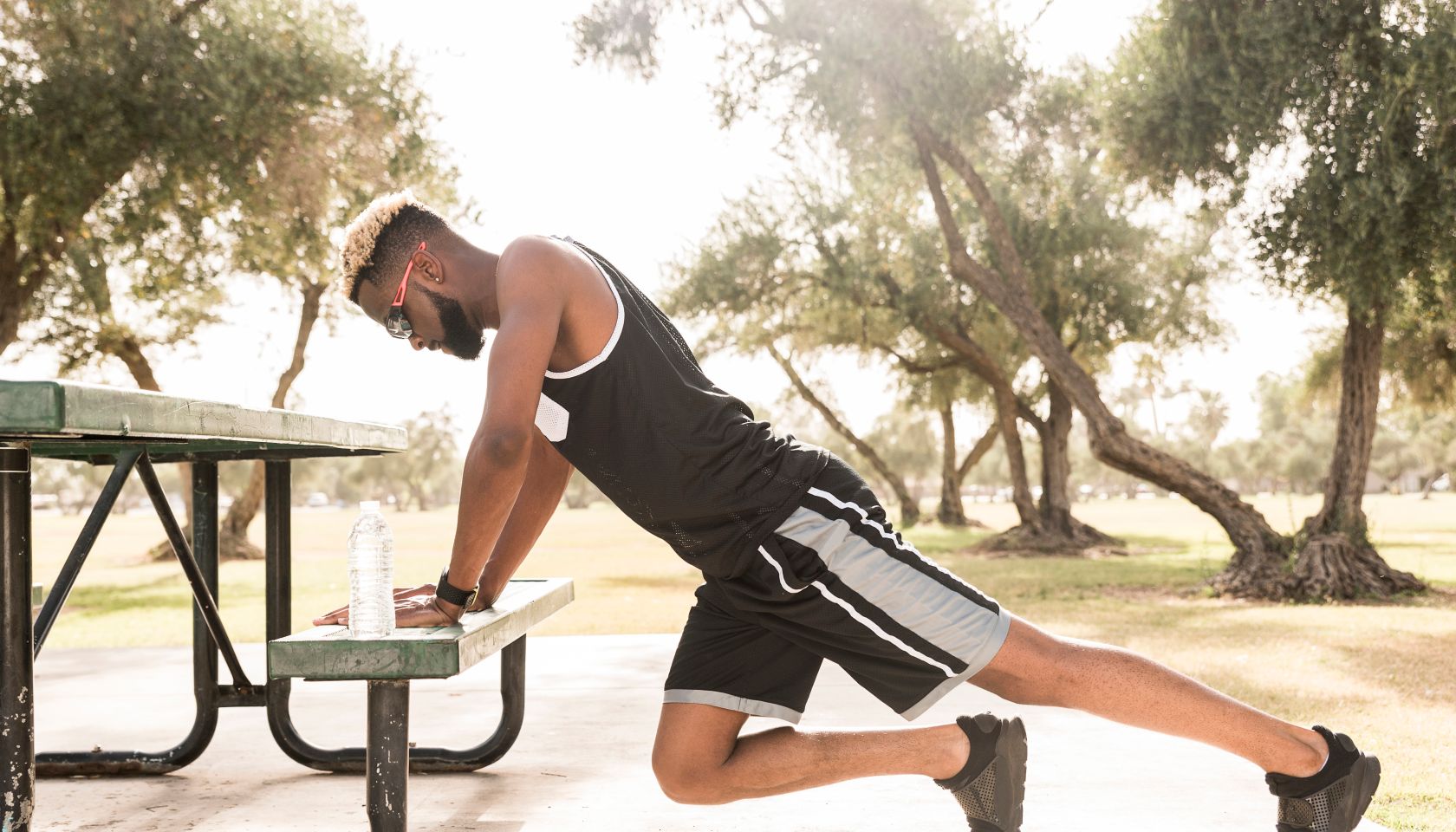 Black man leaning on picnic table in park stretching legs