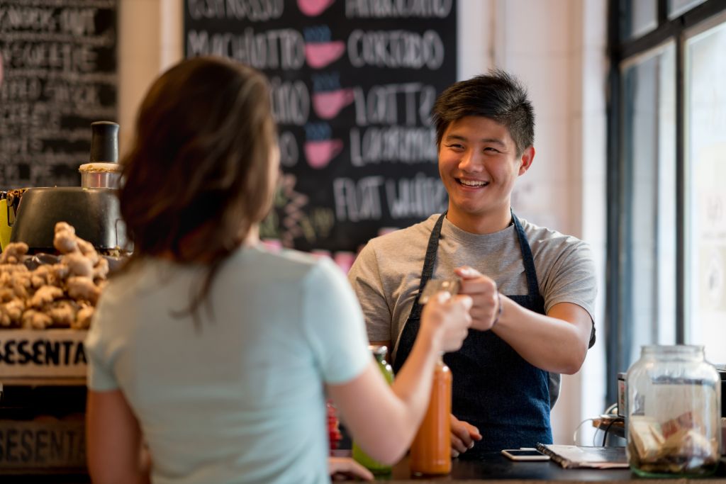 Unrecognizable female customer paying for a juice with a credit card at a juice bar and asian salesman doing the checkout