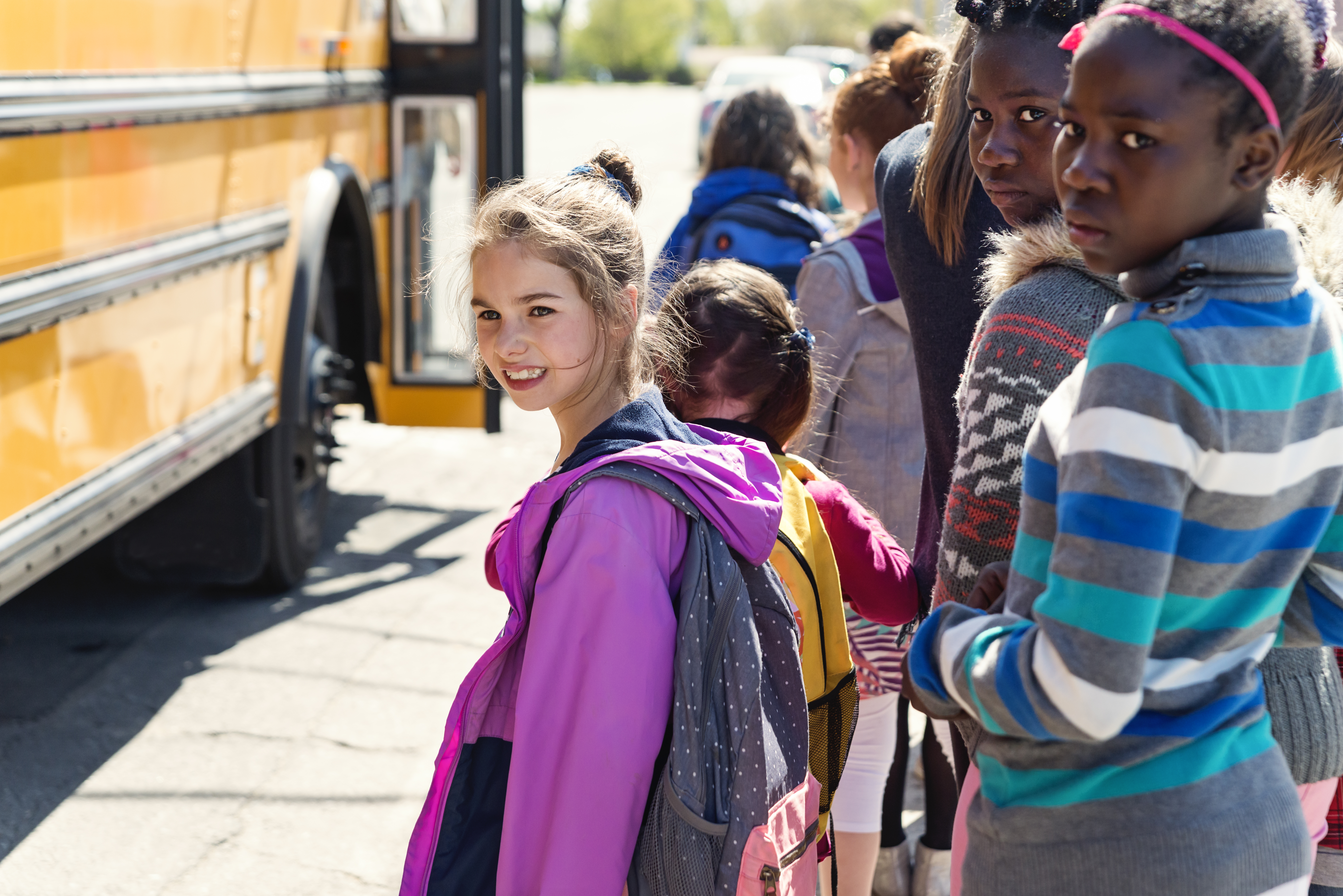 Kids in line waiting to get on school bus saying goodbye.