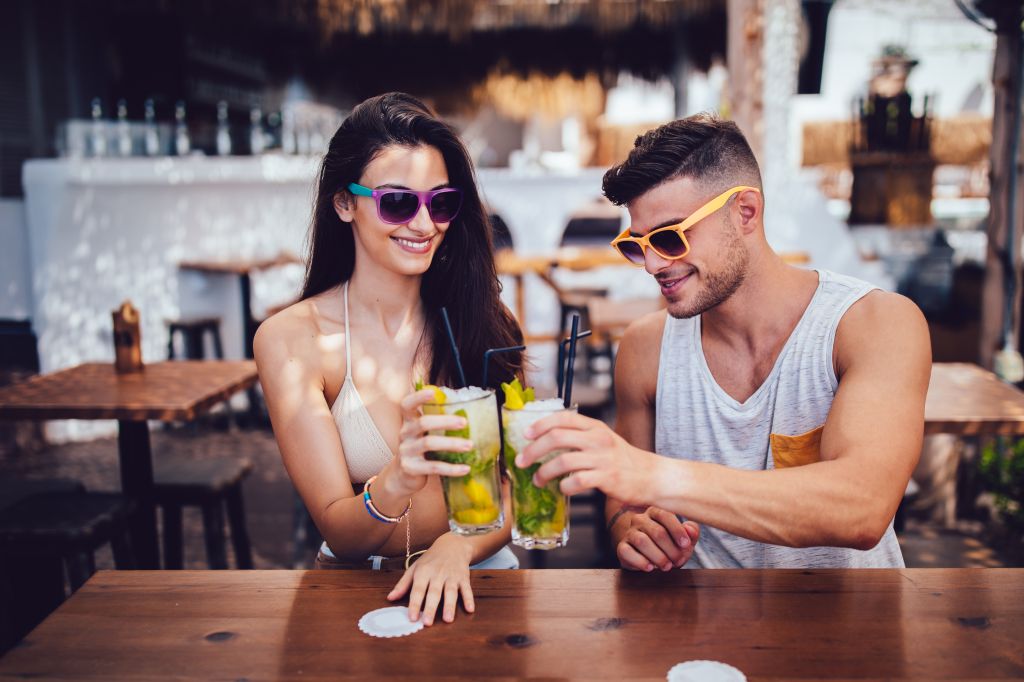 Young hipster couple toasting with cocktails at island summer bar