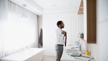 Man putting on tie at mirror in morning bathroom