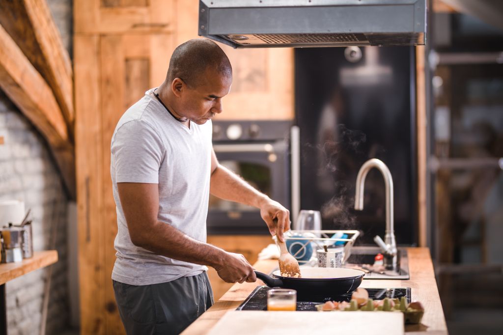 African American bachelor preparing scrambled eggs for breakfast.