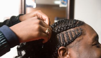 A young man having his cornrows done in the barbers