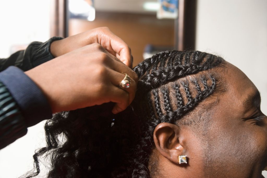 A young man having his cornrows done in the barbers