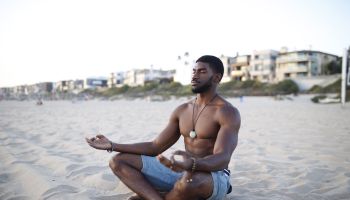 Shirtless Muscular Man Meditating At Beach Against Clear Sky
