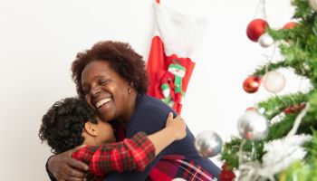 Loving grandmother and grandson hugging very cheerfully standing next to the christmas tree