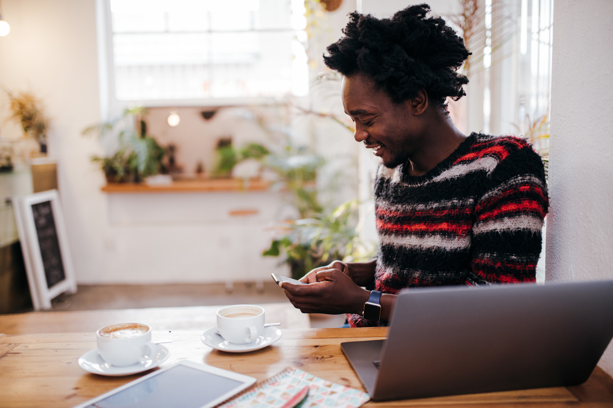 Smiling Man Using Phone By Laptop On Table