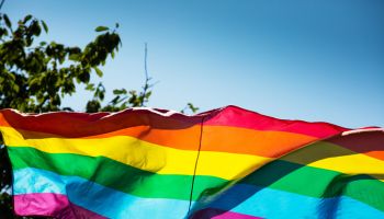 Low Angle View Of Rainbow Flag Waving Against Clear Blue Sky