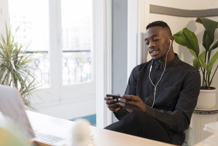 Portrait of young businessman using smartphone and earphones in the office