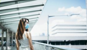 Young Asian woman wearing a protective face mask to protect and prevent from the spread of viruses in the city, looking far away while walking along the city bridge in downtown district