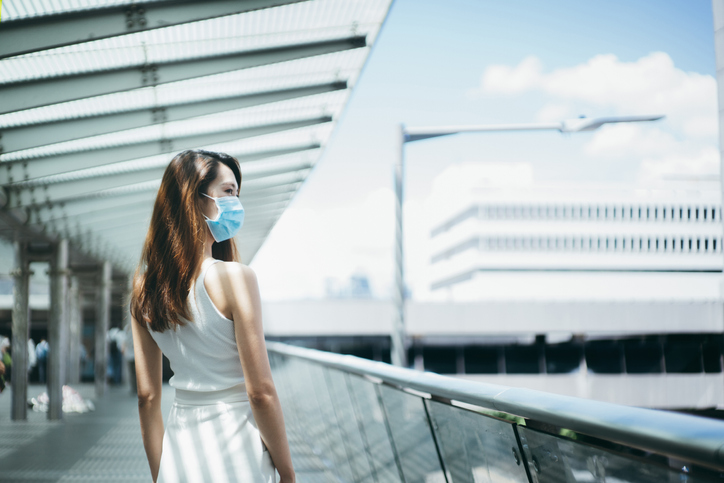 Young Asian woman wearing a protective face mask to protect and prevent from the spread of viruses in the city, looking far away while walking along the city bridge in downtown district