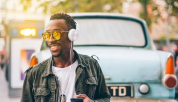 Smiling young man wearing sunglasses listening music through headphones against vintage car in city