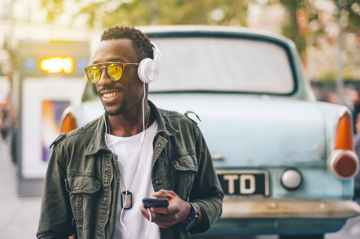 Smiling young man wearing sunglasses listening music through headphones against vintage car in city
