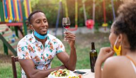 Afro Couple wearing protective face mask having staycation romantic dinner on back yard, during COVID-19