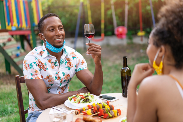 Afro Couple wearing protective face mask having staycation romantic dinner on back yard, during COVID-19