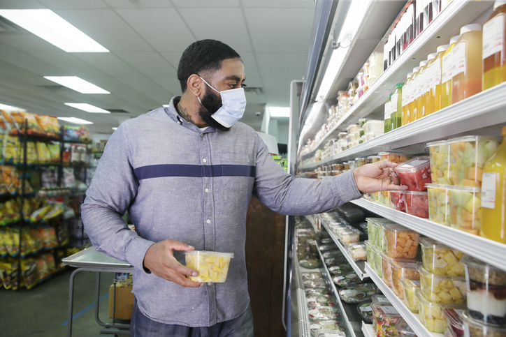 An African-American man wears a surgical mask over his face while shopping at a grocery store.
