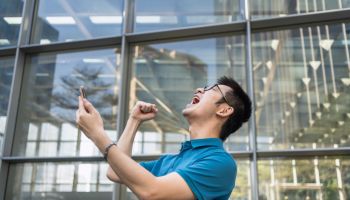 Excited Young Man cheering While Holding Mobile Phone