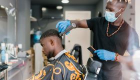 Barber with locs wearing mask and glove while cutting customer's hair in salon