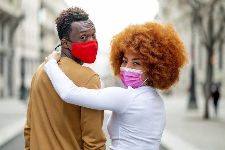 Woman wearing face mask with arm around on man standing outdoors