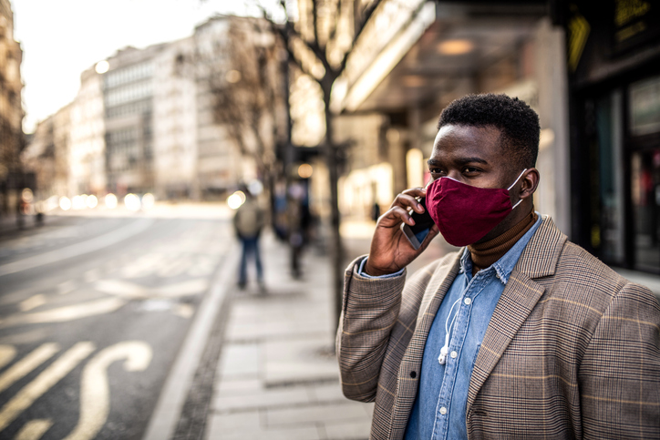 African American man waiting for a bus in the city with face mask on.