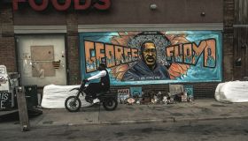 A man rides a motorcycle next to a mural of George Floyd by...