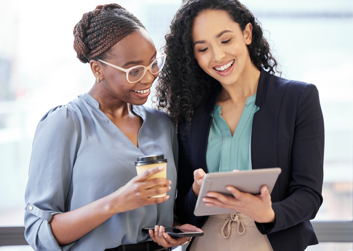 Cropped shot of two attractive young businesswomen looking a tablet while standing in the office